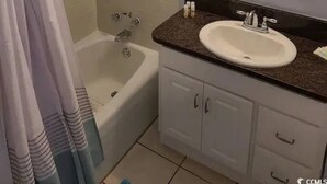 A bathroom with a bathtub, a sink with a mirror above it, and a shower curtain.