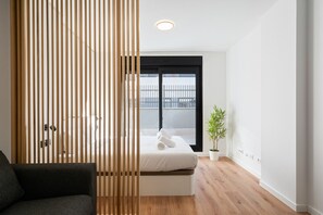 Une chambre moderne avec un lit, une cloison en bois, une plante en pot et une vue sur l’extérieur.