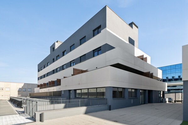 Un immeuble moderne à plusieurs étages, doté d’un toit plat, de grandes fenêtres et d’une entrée sécurisée par un portail.