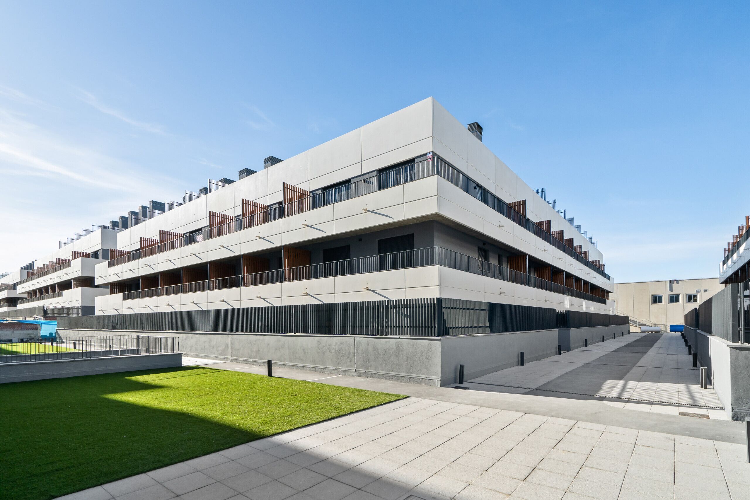 Een modern meerijlaarig gebouw met een plat dak, grote ramen en een centrale binnenplaats met een gazon.