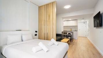 Een moderne hotelkamer met een groot bed, een houten scheidingswand, een kitchenette en een aan de muur bevestigde televisie.
