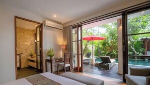 A bedroom with a large bed, a desk, and a chair. There is a view of an outdoor area with a pool and lounge chairs. - Pulung Villa (Bali)