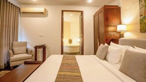 A hotel room with a large bed, a chair, a desk, and a bathroom visible through an open door. - Pulung Villa (Bali)