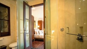 A bathroom with a glass shower enclosure, a toilet, and a bed visible through an open door. - Pulung Villa (Bali)