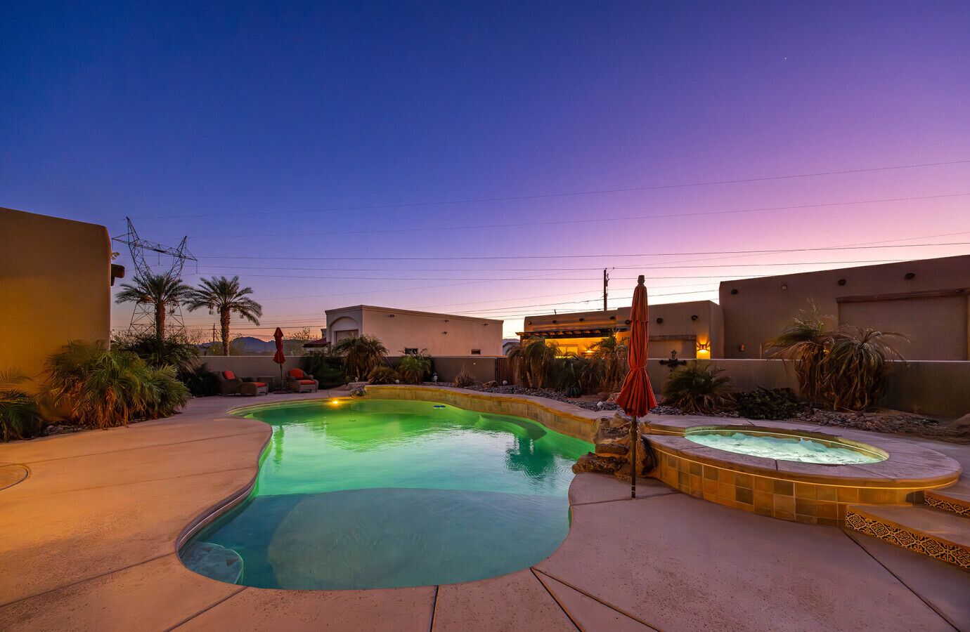 Una piscina con idromassaggio, circondata da palme e un cielo al tramonto.