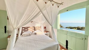 A bed with a white canopy, a wooden headboard, and a view of the sea through an open door.