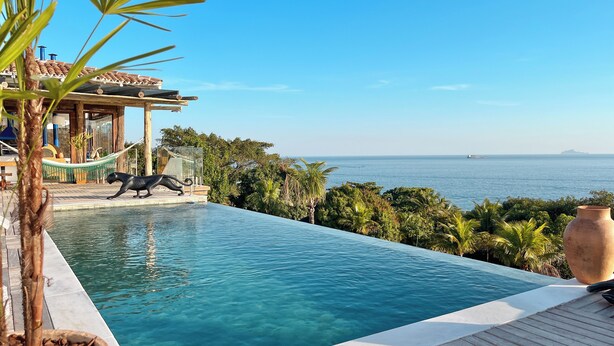 A clear blue pool with a wooden deck, a hammock, and a view of the sea.