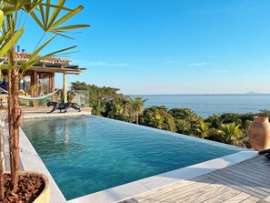 A clear blue pool with a wooden deck, a hammock, and a view of the sea. - Blow Show Casa III Guest House (Ilhabela)