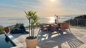 A wooden deck with a table and chairs, overlooking a body of water and distant mountains.