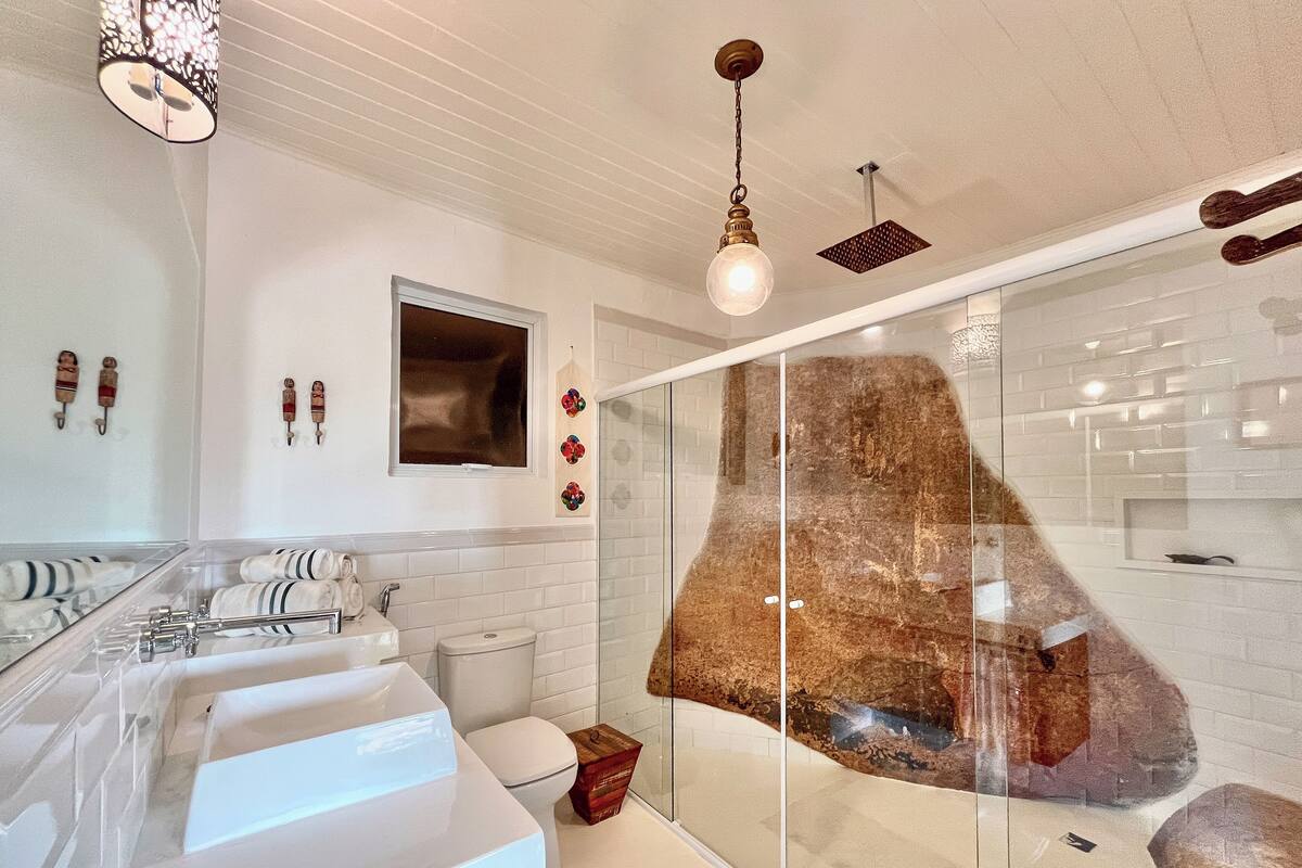 Un baño moderno con un espejo grande, varios lavamanos, una cabina de ducha de vidrio y arte decorativo en la pared.