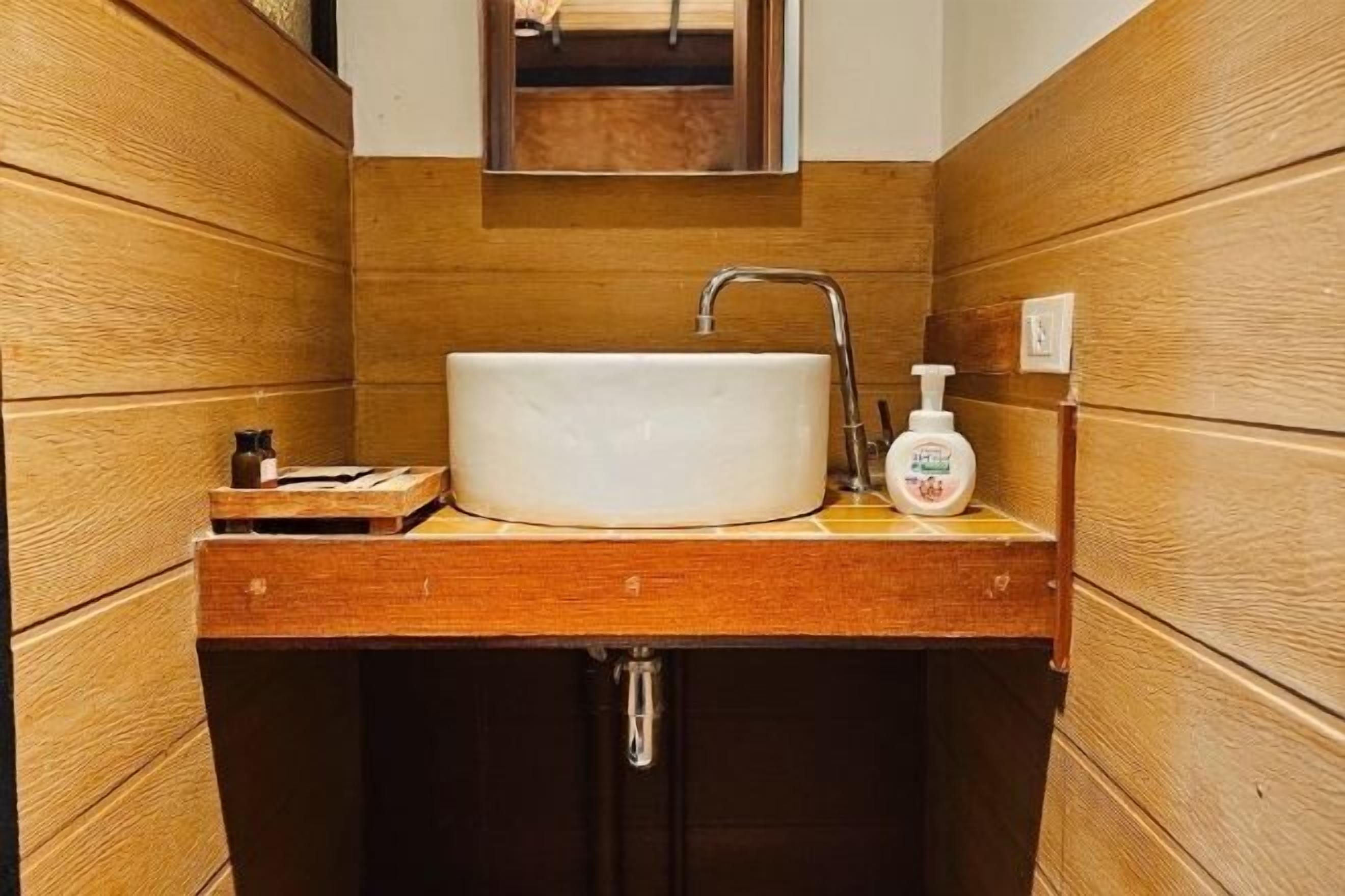 Ein Badezimmer mit einem Holzkosmetikschrank, einem weißen Waschbecken, einem Wasserhahn und einer Seifenspender.