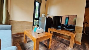 A room with a wooden floor, a sofa, a wooden coffee table, a television on a wooden stand, and a window with curtains. - R1 Resort Rajapruek Chiangmai (Hang Dong)