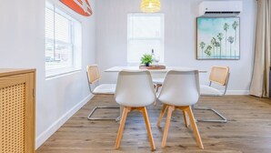 Zona pranzo moderna con tavolo bianco, due sedie, una lampada a sospensione e un quadro raffigurante palme al muro.