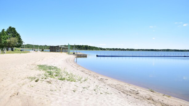 Ein sandiger Strand mit einem ruhigen See, einer Holzsteg und eine Reihe von blauen Pontons.