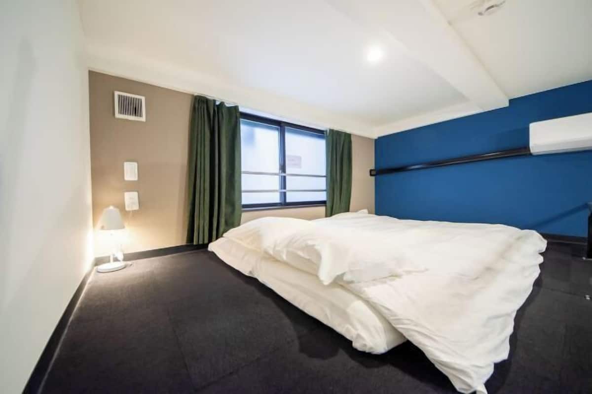 A hotel room with a bed, a window with curtains, a wall-mounted air conditioner, and a lamp.