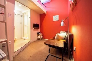A compact room with a wooden desk, a chair, a bed, a small TV, and a bedside lamp. - Apartment Sanjo (Nara City)