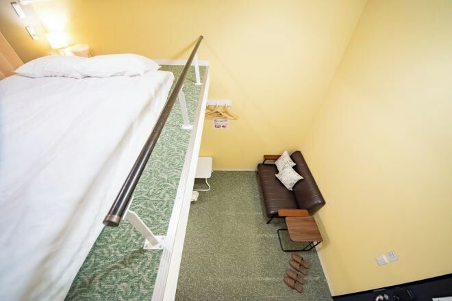 A room with a bed, a sofa, a small table, and a wall-mounted shelf.