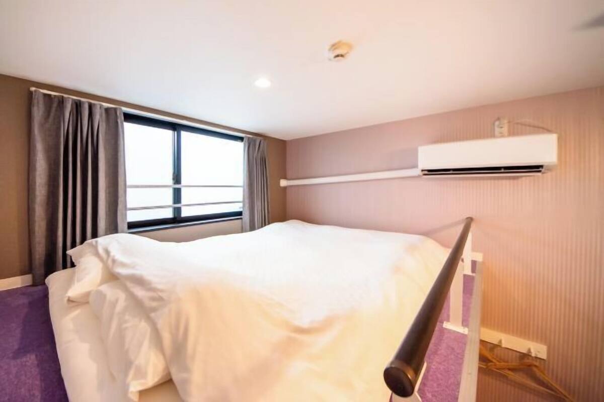 A hotel room with a bed, window, air conditioning unit, and a curtain.