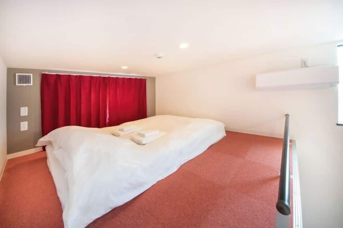 A single bed with white bedding, a red curtain, a white wall, and a red carpeted floor.