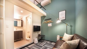 A compact living space with a kitchenette, a sofa, a TV, and a wall-mounted lamp. - Apartment Sanjo (Nara City)