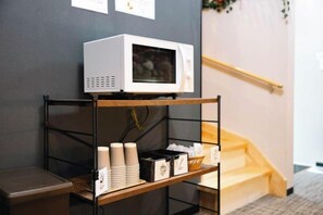 A microwave on a shelf, stacked cups, and a small table with a tray. - Apartment Sanjo (Nara City)