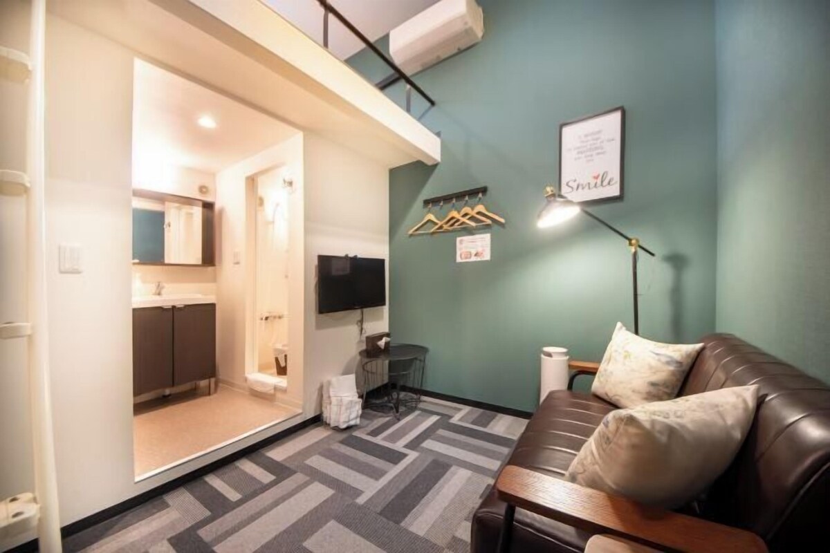 A compact living space with a kitchenette, a sofa, a small table, and a mounted TV.