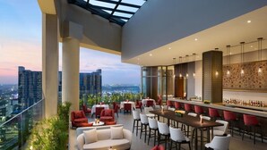 A modern rooftop bar with a city view, featuring red and white seating, a long bar, and ambient lighting. - The Leela Bhartiya City Bengaluru (Bengaluru)