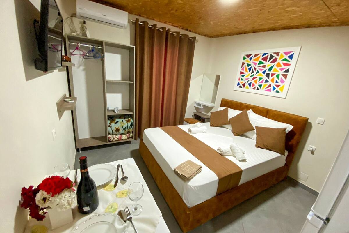 A hotel room with a bed, a table set for dining, a wardrobe, and a bathroom visible through an open door.