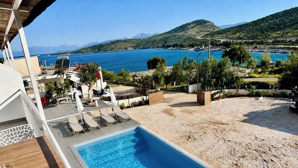 A swimming pool with lounge chairs, a view of the sea, and a hilly landscape in the background.