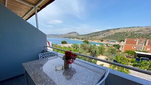 A balcony with a granite table, a vase with flowers, and a view of a coastal landscape.