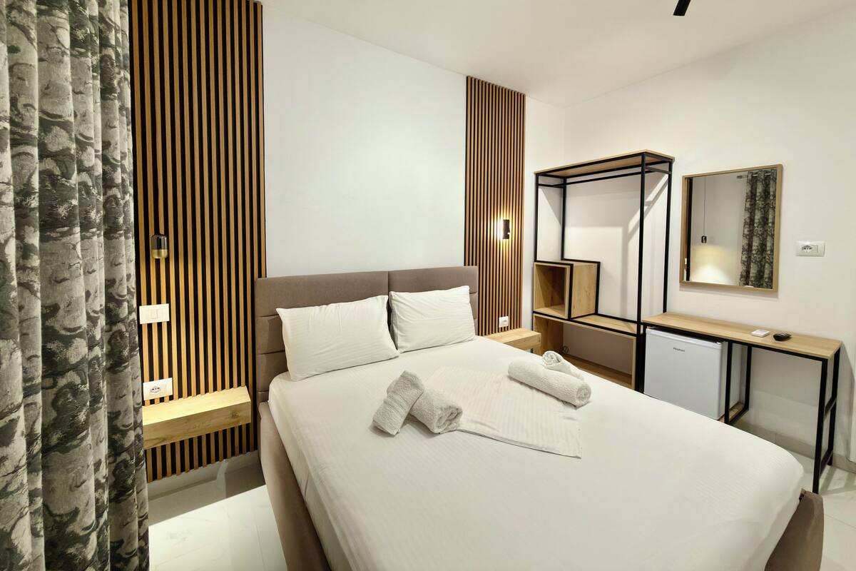 A modern hotel room with a bed, bedside tables, a desk, and a mirror.