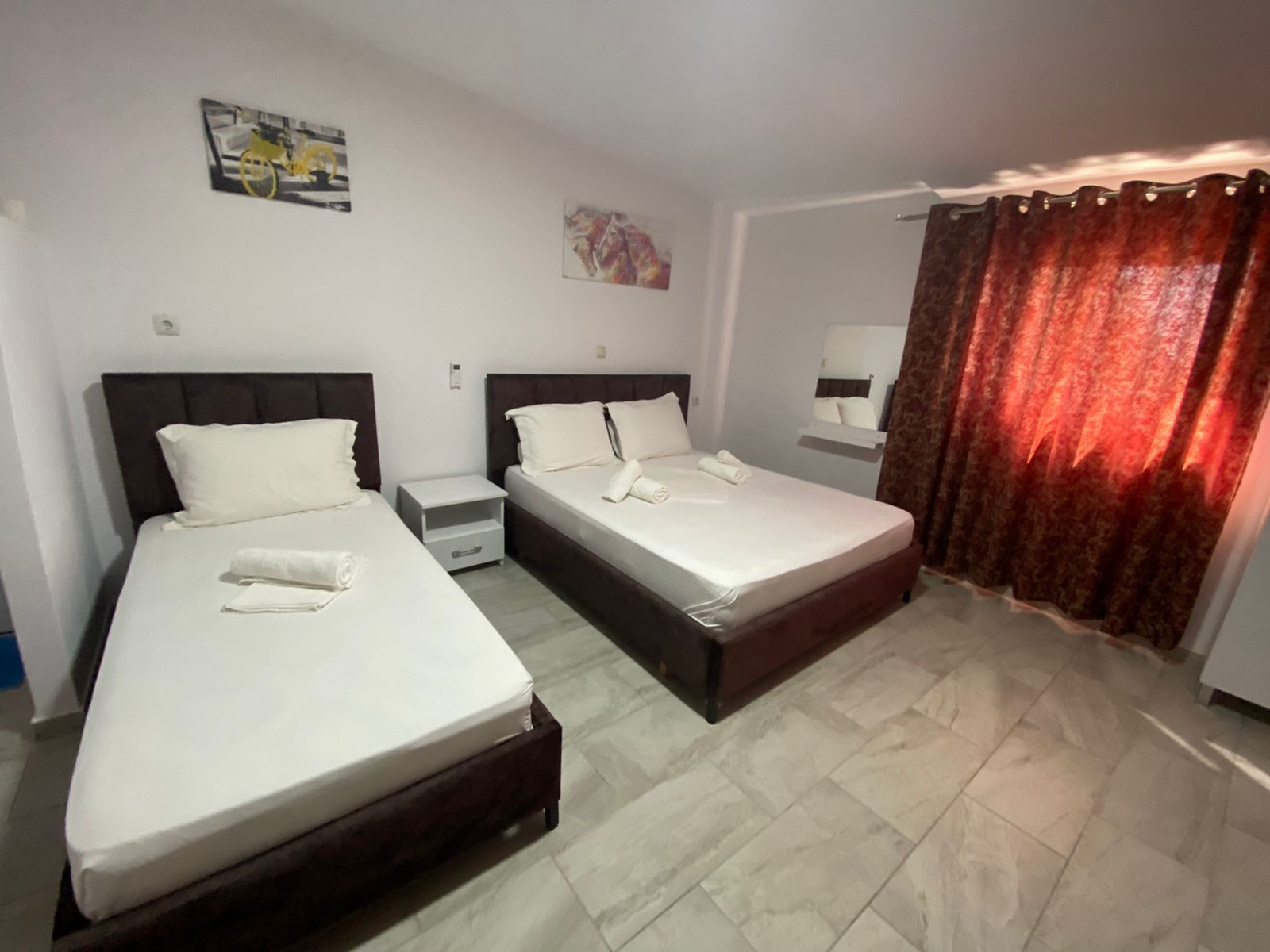 A hotel room with two beds, a nightstand, a mirror, and a red curtain.