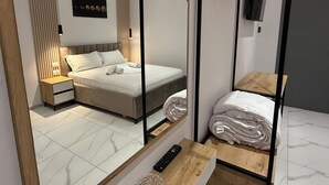 A modern hotel room with a bed, bedside tables, a mirror, and a wooden dresser.