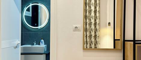 Une salle de bain avec un miroir rond, un lavabo, des toilettes et un rideau de douche.