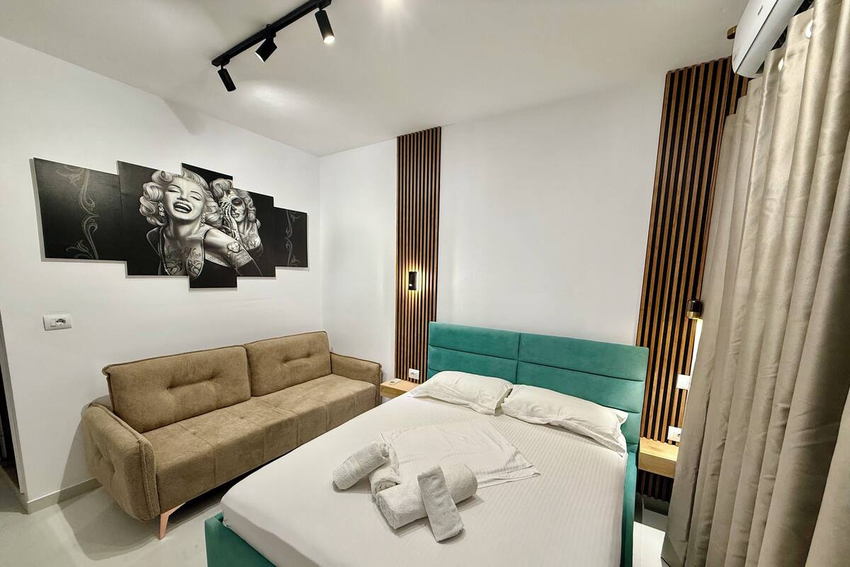 A modern bedroom with a bed, a sofa, and a wall-mounted light fixture.
