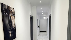 A modern hallway with white walls, a marble floor, and a potted plant on a shelf.