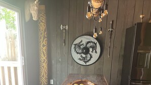 A rustic wooden table with a bowl of fruit, a decorative wall with a horse head and a circular design, and a hanging light fixture. - Kings Court (Dalton)