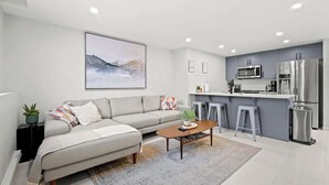 A modern living room with a sofa, coffee table, and a kitchen area with a microwave and refrigerator. - King Bed Mtn Escape Free Parking 1hr to Banff (Calgary)