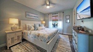 A bedroom with a bed, bedside tables, a ceiling fan, a window with curtains, and a wall-mounted TV. - Sleeps 18 2 Beachfront Condos w/ 2 Pools, Tennis/pickleball, Beach Boardwalk (Port Aransas)