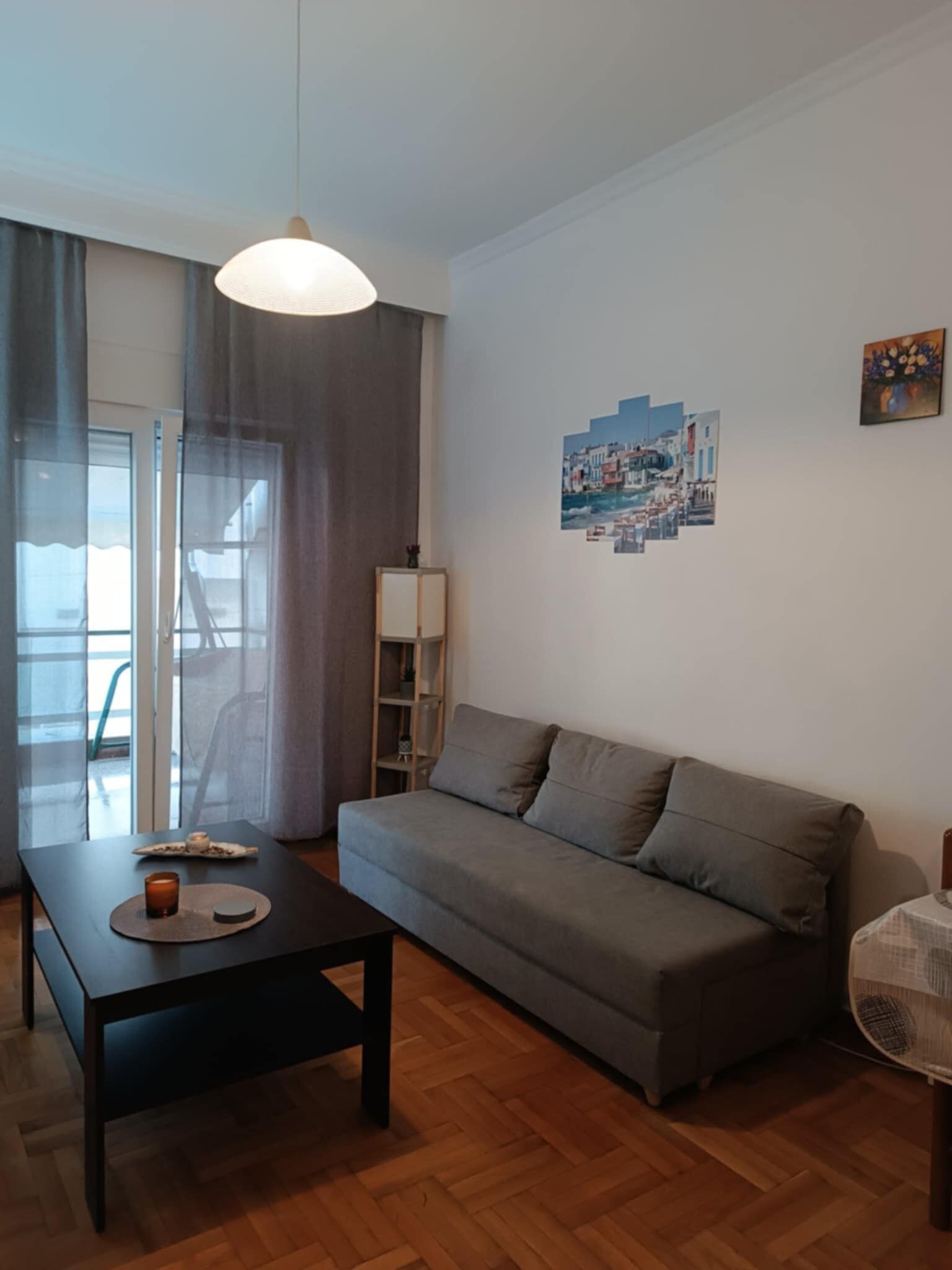 Ein Wohnzimmer mit grauem Sofa, einem schwarzen Couchtisch, einer Lampe, einem Gemälde und einem Ventilator.