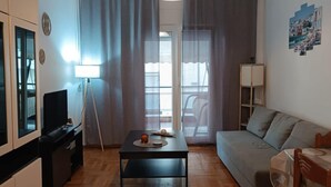 Ein modernes Wohnzimmer mit Holzdielenmuster-Boden, einem schwarzen Couchtisch, einem grauen Sofa, einem Fernseher und einer Lampe.