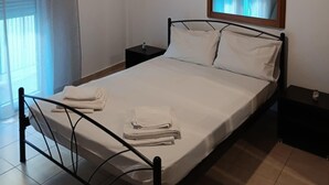 Ein Einzelbett mit Metallgestell, ein Nachttisch, eine Lampe an der Wand und ein Fenster mit Jalousien.