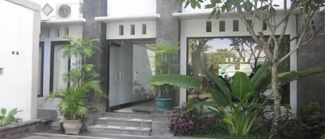 Un edificio moderno con entrada principal, plantas en macetas y un área pavimentada con diseño decorativo.