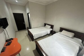 Ein Hotelzimmer mit zwei Betten, einem kleinen orangefarbenen Tisch mit Fernbedienung und einem an der Wand befestigten Fernseher.