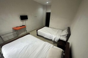 Ein Hotelzimmer mit zwei Einzelbetten, einem Fernseher, einem kleinen orangefarbenen Tisch und einem Nachttisch.