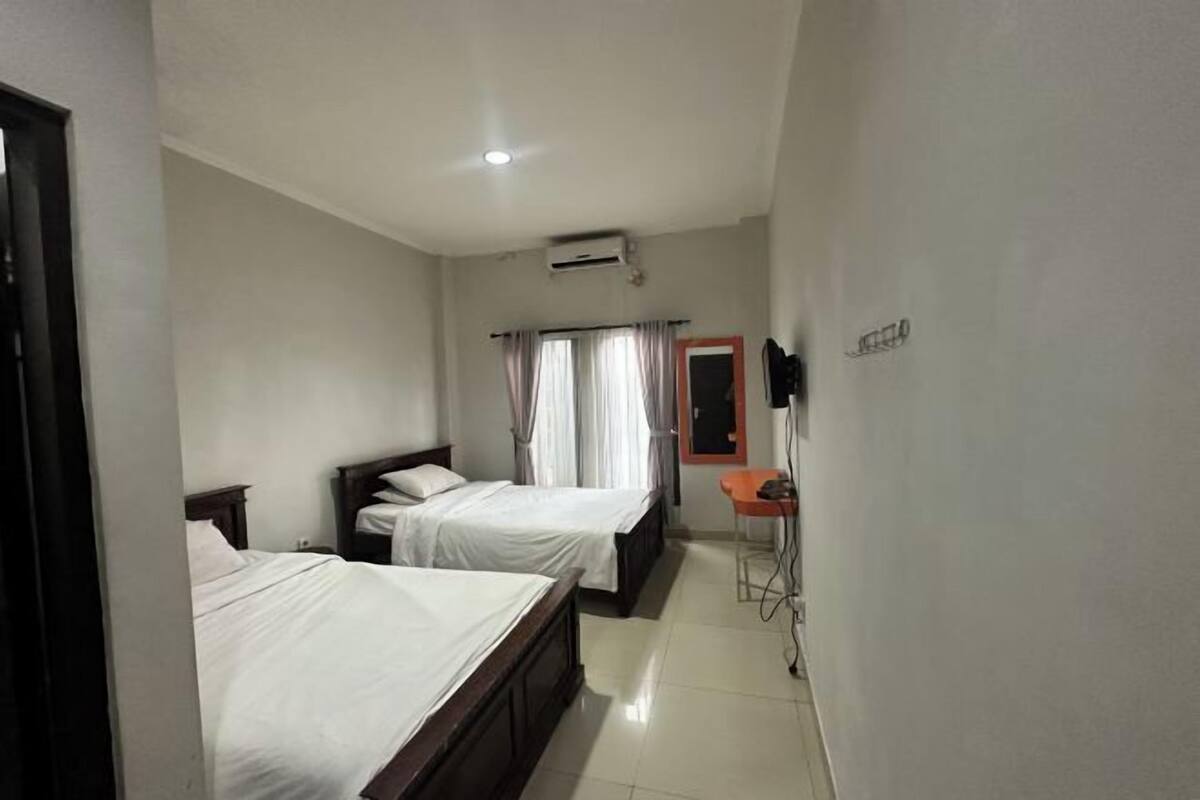 A hotel room with two beds, a small table, a chair, an air conditioning unit, and a TV mounted on the wall.