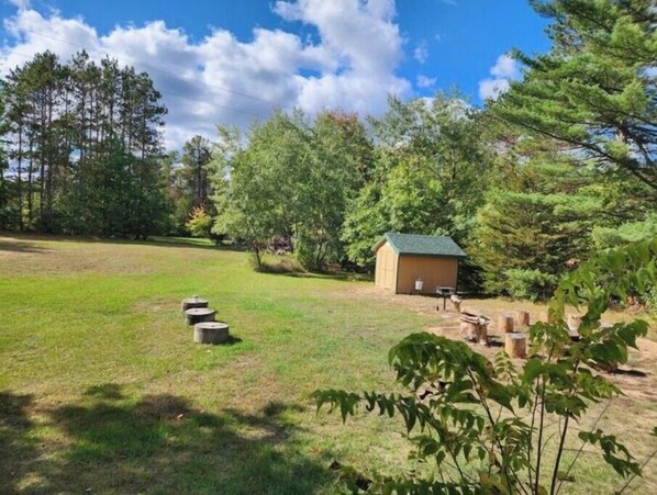 A grassy outdoor area with a small wooden shed, a fire pit, and a bench. - Close Counts when you're playing any season. (Wisconsin Dells)