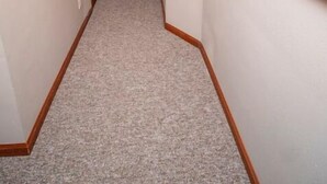 Um corredor com piso coberto de carpete, um quadro na parede direita e um relógio na parede esquerda.