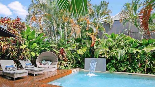 A pool area with a wooden deck, lounge chairs, and a waterfall feature surrounded by lush tropical plants. - Mantra on the Inlet Port Douglas (Port Douglas)