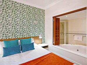 A hotel room with a bed, a nightstand, a lamp, a bathroom with a shower and a bathtub, and a large mirror. - Mantra on the Inlet Port Douglas (Port Douglas)